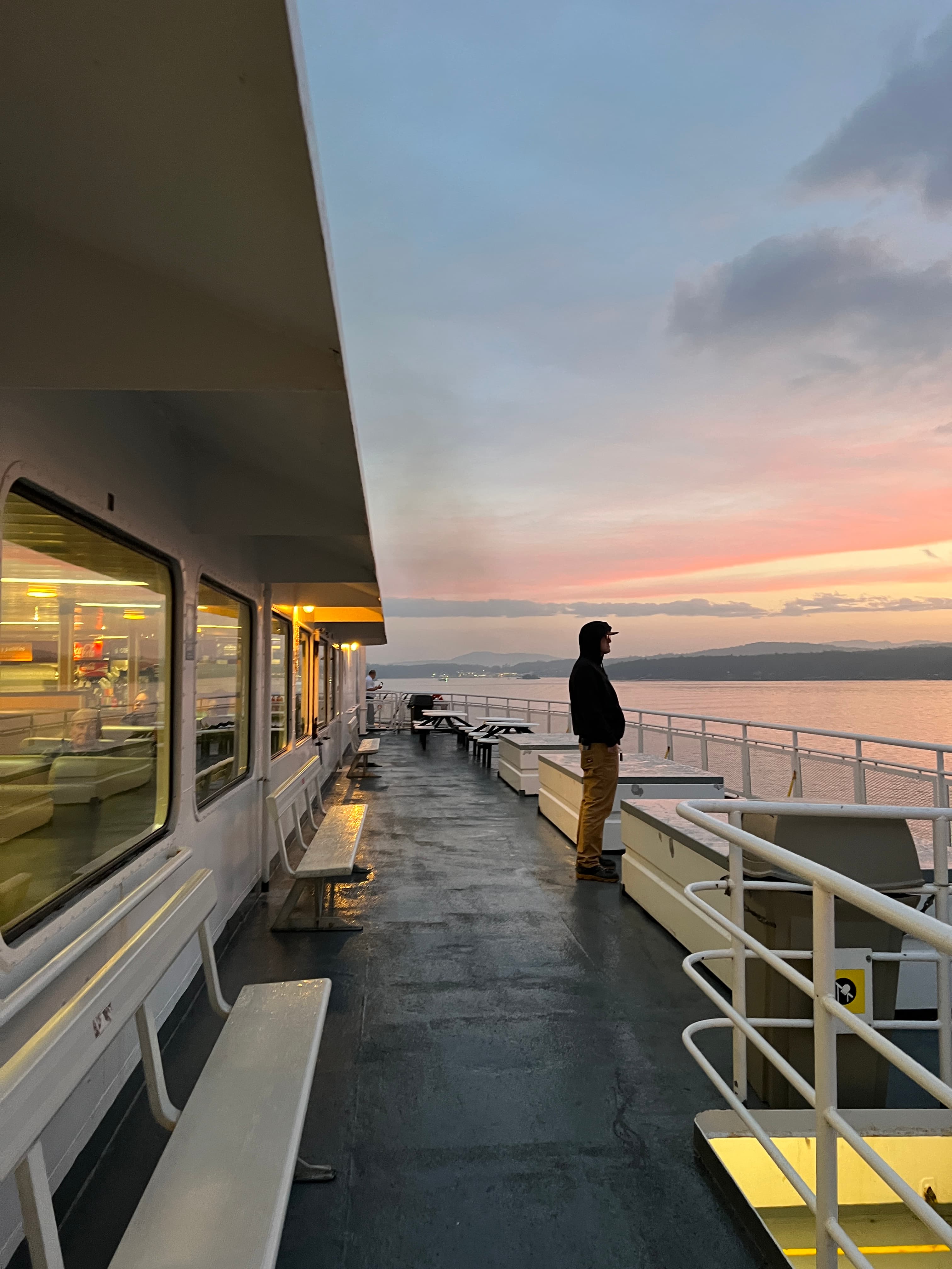 Person standing on a ferry deck during sunset over the water