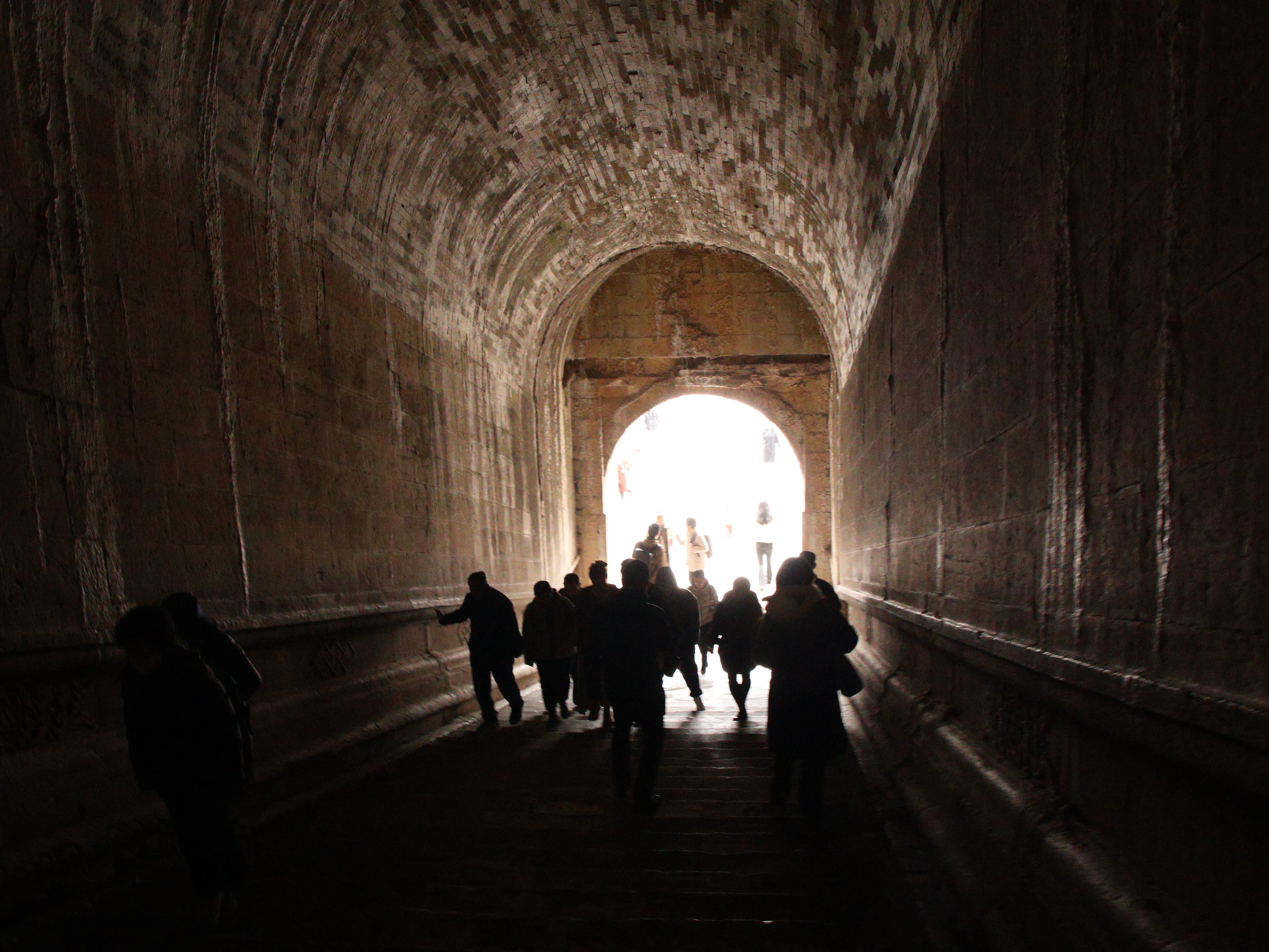 Silhouettes of people walking through an arched tunnel toward bright light